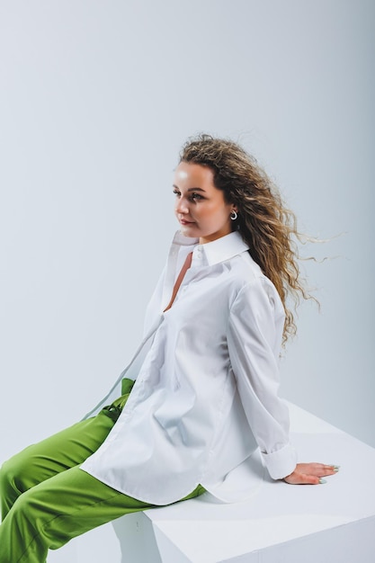Positive woman with curly hair in a white light cotton shirt and trousers on a white isolated background Women's casual wear