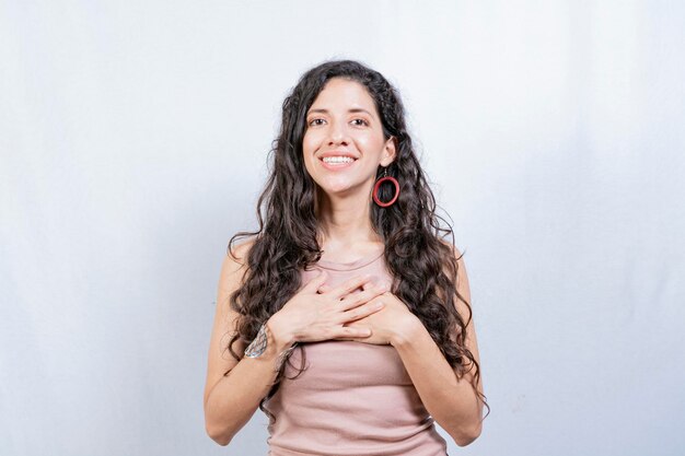 Positive woman with lovely sincere smile feeling thankful relaxed person showing thank you gesture with hands on chest Grateful people concept