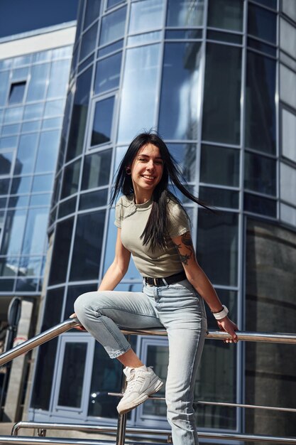 Positive woman with tattoo on arm have fun outdoors against business building at sunny daytime