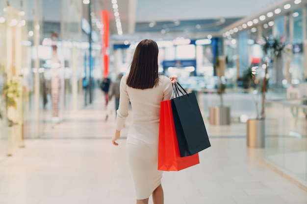 Positive young adult woman carrying paper shopping bags in hands. Rear back view