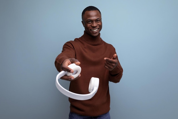 Positive young african male consultant holding out headphones to the camera on the background with