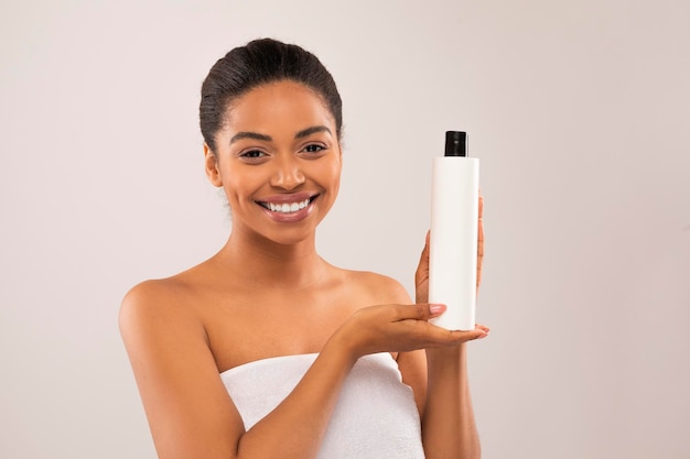 Positive young african woman holding bottle with beauty product