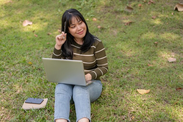 A positive young Asian female college student working remotely at a campus park