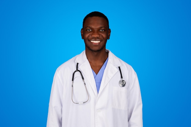 Photo positive young black guy doctor in white coat enjoy work isolated on blue studio background