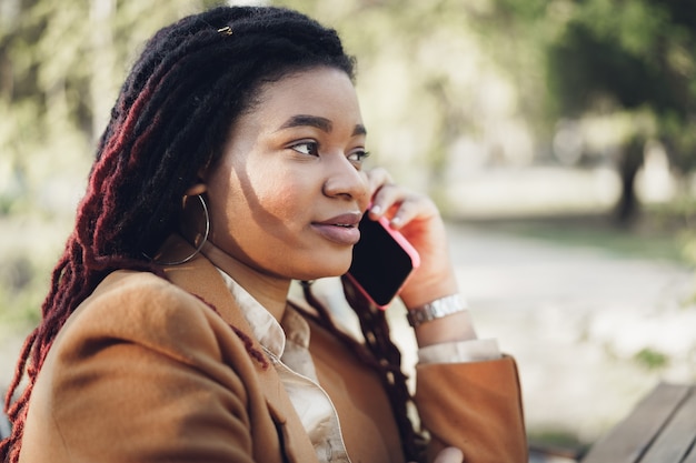 Positive young black woman sitting in outdoor cafe and takling on the phone