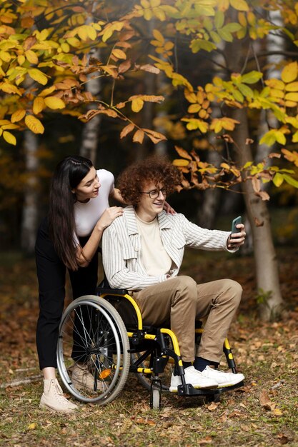 Positive young boy and girl outdoors A guy sits in a wheelchair takes a selfie with his girlfriend