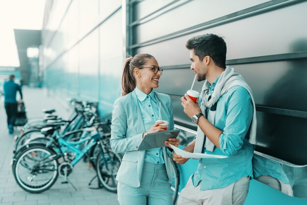 陽気な若いビジネスマンが屋外に立って、議論して、コーヒーを飲みに行きます。