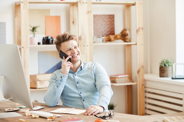 Positive young entrepreneur discussing project on phone