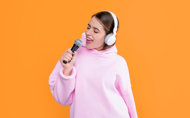 Positive young girl in headphones with microphone on yellow background
