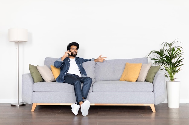 Positive young indian guy chilling on couch have phone call