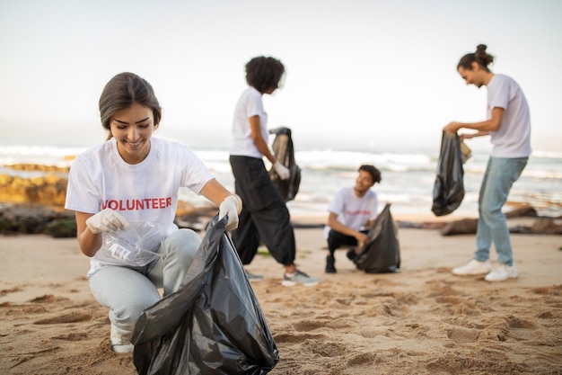 Positive young international people volunteers in gloves and european lady with garbage bags clean