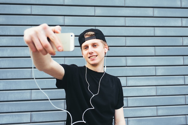 Positive young man in a cap and a black T-shirt makes selfie