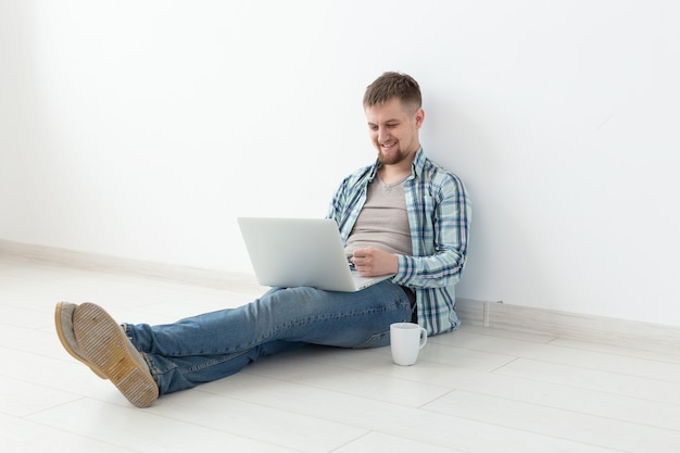 Positive young man in casual clothes and glasses surfing the internet using wifi and a laptop in