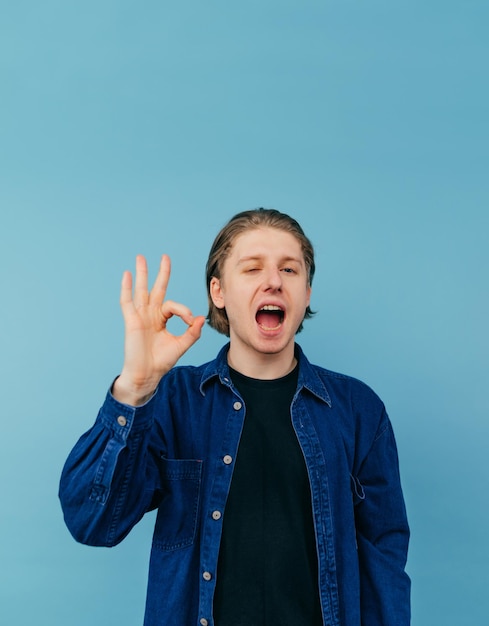 Positive young man in casual clothes stands on a blue background with a smile on his face