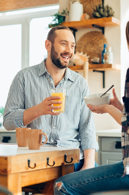 Positive young man holding a glass of juice and smiling to a girlfriend