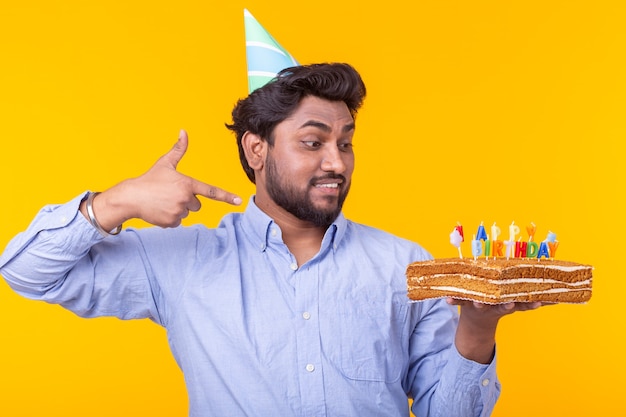 노란색 벽에 포즈 생일 케이크를 들고 긍정적 인 젊은 남자.