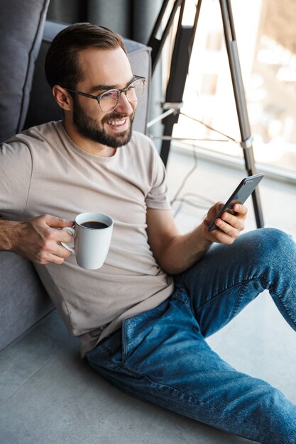 家の中で携帯電話を使ってコーヒーを飲んでいる前向きな若者。