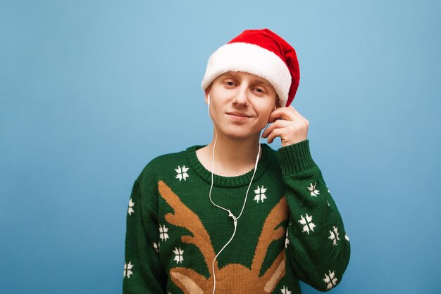 Positive young man listening to Christmas music on blue background