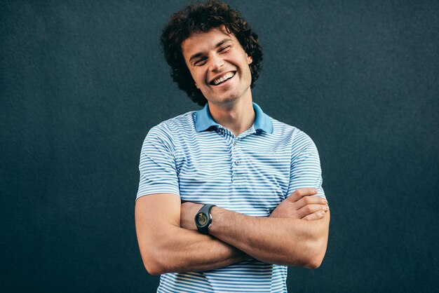 Positive young man posing for advertisement smiling and looking at the camera standing at building wall outdoors Portrait of happy smart student male has positive expression People and emotion