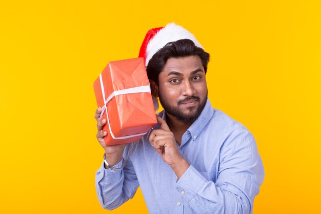 Positive young man Santa Claus with gifts and Christmas tree posing on a yellow wall. Christmas holidays concept.