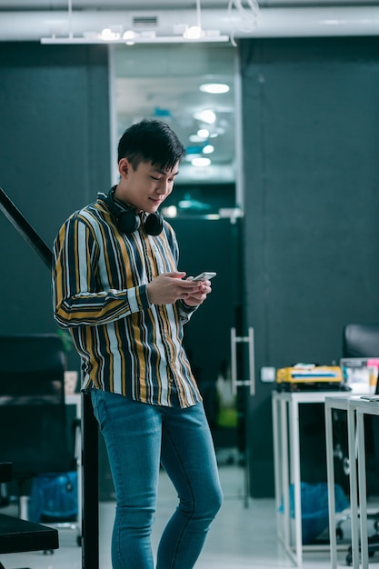 Positive young man standing by the banister and looking at the screen of smartphone