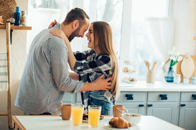 Positive young man and woman hugging and smiling in excitement while being in the kitchen