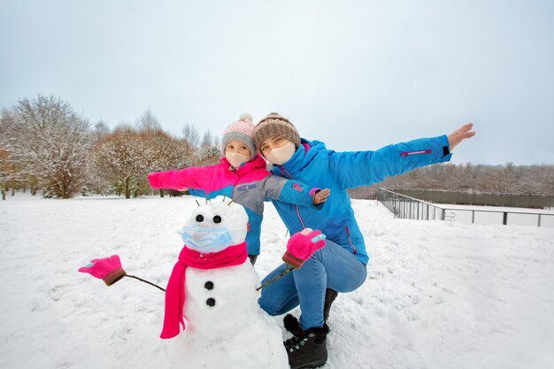 ポジティブな若い母親と娘は、作られたばかりの雪だるまと遊ぶのを楽しんでいます