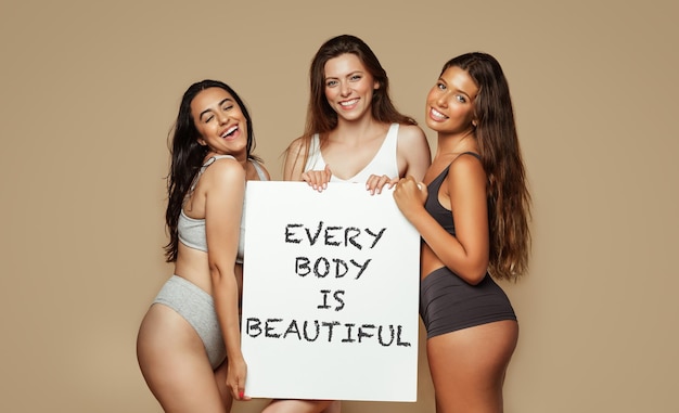 Positive young multiethnic women in different underwear enjoy natural beauty hold banner