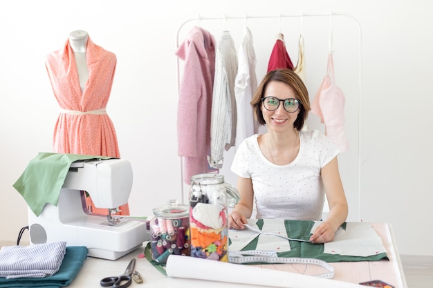 Positive young pretty girl seamstress designer working on a new project while sitting at her desk with a sewing machine in her workshop. Creative business concept.