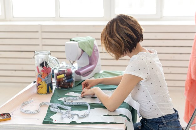 Позитивная молодая красивая девушка-швея-дизайнер работает над новым проектом, сидя за своим столом