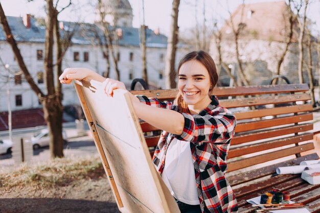 肯定的な若い女性アーティストは、ベンチに座っている間に絵を描きます。