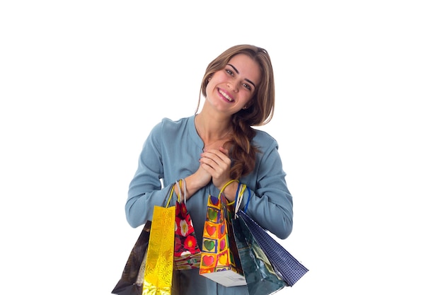 Positive young woman in blue blouse holding shopping bags in her hands on white background in studio