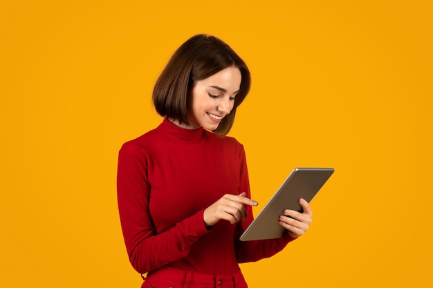 Positive young woman digital nomad using tablet on orange