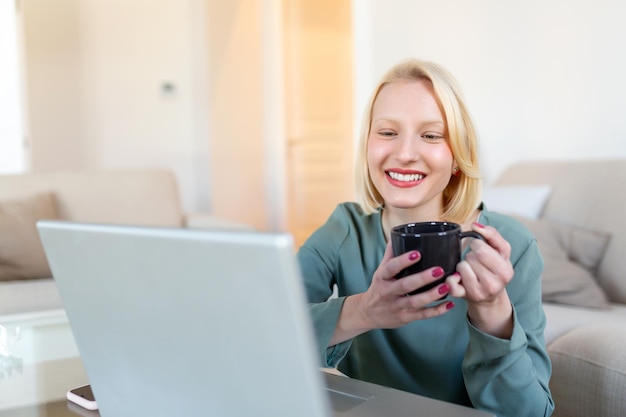 Positive young woman freelancer watching video in blog on netbook and having a coffee at comfortable home Beautiful young business woman working on laptopFreelancer connecting to internet