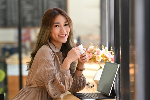 Positive young woman holding coffee cup and smiling at camera