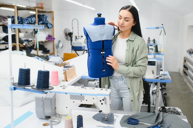 Positive young woman sewing with professional machine at workshop