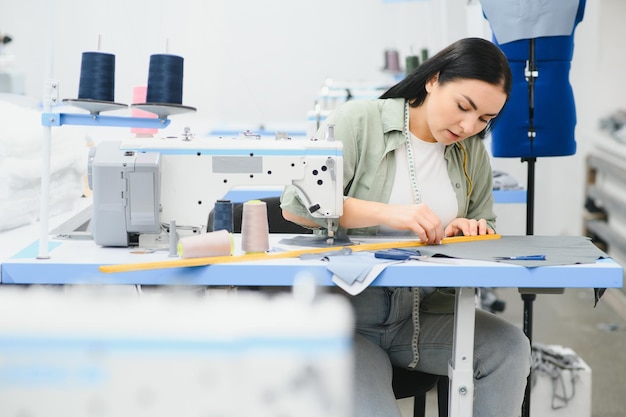 Positive young woman sewing with professional machine at workshop