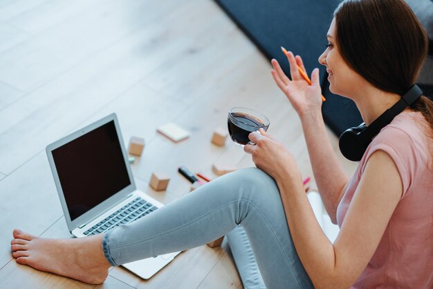 Positive young woman sitting with a cup of coffee on the floor in front of a laptop and gesturing with one hand