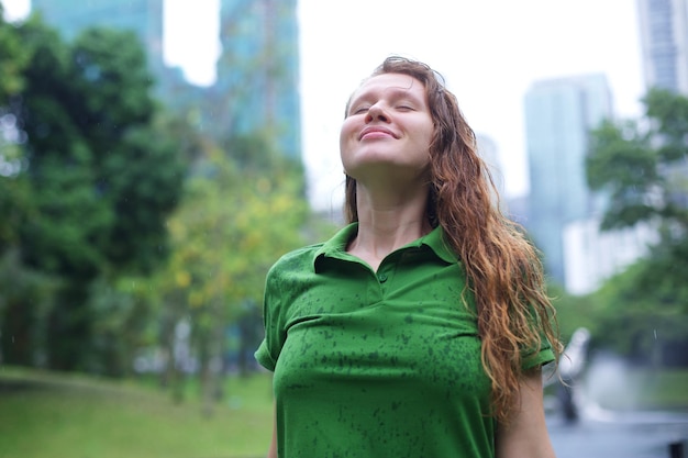 야외에서 비를 즐기는 공원 쾌활한 여성에 비가 동안 웃는 긍정적 인 젊은 여자