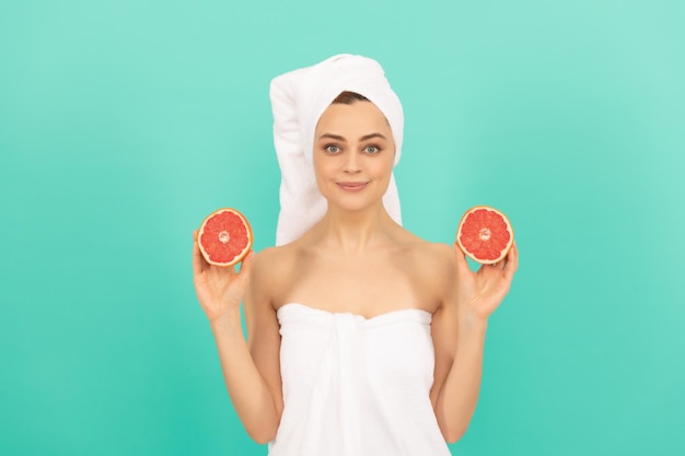 Positive young woman in towel after shower with grapefruit on blue background