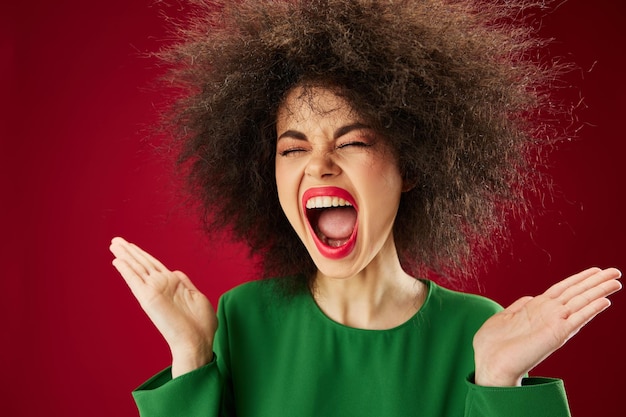 Positive young woman with curly hair grimace posing emotion red background unaltered High quality photo