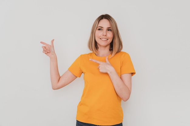 Positive young woman in yellow t-shirt pointing her finger to the side. On white background. Hand gestures