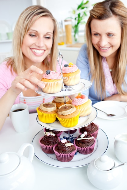 Photo positive young women eating cakes in the kitchen