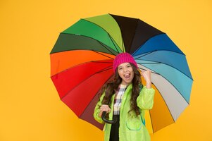 Фото Концепция позитива дождливый день веселья счастливая прогулка под зонтиком наслаждайтесь концепцией дождя малышка с удовольствием держит красочный радужный зонтик дождливая погода с подходящей одеждой яркий зонтик веселитесь
