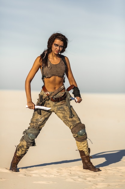 Post-apocalyptic woman warrior with weapon outdoors. Attractive fichter girl in shabby clothes