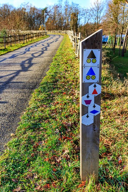 Post met wandel- en fietspadborden aan de zijkant van een pad tussen houten hekken richting hoge kempen nationaal park kale bomen op zonnige herfstdag op de achtergrond in as limburg belgië