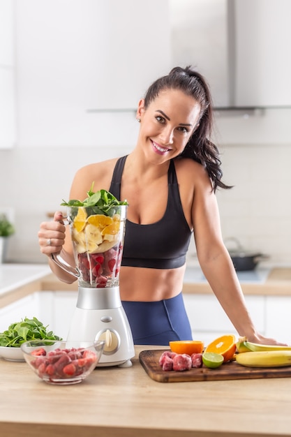 Post-workout nutrition for a woman in fitness clothes in a form of red berries, oranges and spinach in a blender.