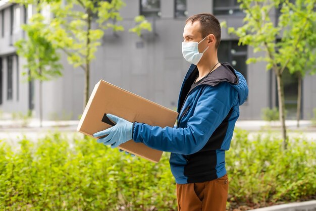 Postbezorger die een beschermend gezichtsmasker draagt voor een bestelwagen die een pakketdoos aflevert als gevolg van de ziekte van coronavirus of covid-19.