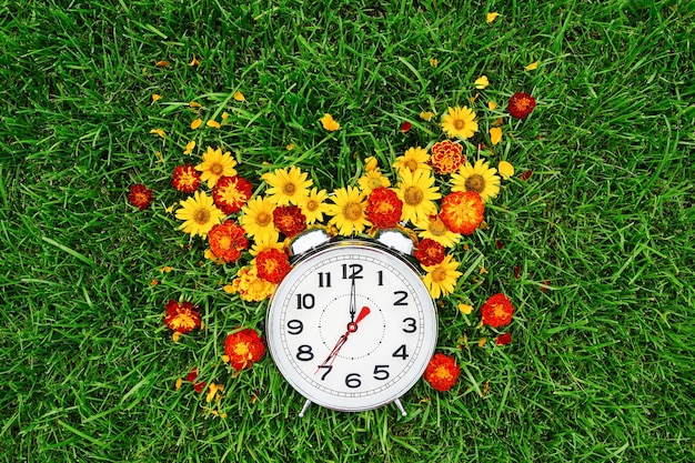 Postcard good morning and alarm clock with yellow and red flowers lie on the green grass