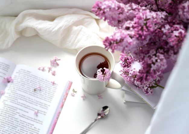 The postcard is beautiful A mug of tea an old book and a bouquet of purple lilac A beautiful still life Spring time The concept of Good morning